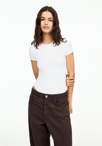 Body alb cu mânecă scurtă, combinat cu pantaloni închiși la culoare, cu talie înaltă. Material neted, cu un design ajustat și detalii minimalistice.