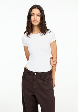 White short-sleeve bodysuit paired with dark brown high-waisted pants. Smooth material with a fitted design and minimalist details.