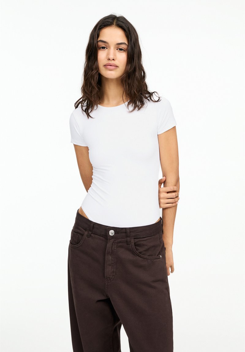 Body alb cu mânecă scurtă, combinat cu pantaloni închiși la culoare, cu talie înaltă. Material neted, cu un design ajustat și detalii minimalistice.