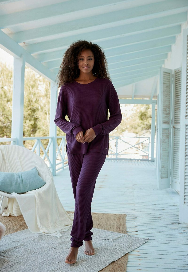 Lila Waffelstrick-Loungewear-Set mit einem langärmeligen Oberteil und schmal zulaufenden Hosen, in lockerer Passform und mit gerippten Bündchen. Heller Hintergrund.