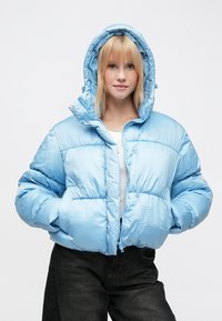 Svetlomodrá nadýchaná bunda s podšitou kapucňou, zapínaním na zips a elastickými manžetami. Hladká, lesklá látka s prešívaným vzorom a bočnými vreckami.