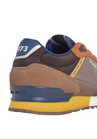 Rudos ir pilki sportbačiai su zomšiniais ir sintetiniais viršutiniais audiniais, mėlynais akcentais, geltonu padu ir numeriu "973" ant kulno. Yra Pepe Jeans prekės ženklas.