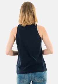 Top sin mangas de color azul marino hecho de una tela suave y texturizada. Presenta un escote redondo y un corte relajado, combinado con jeans de color azul claro.