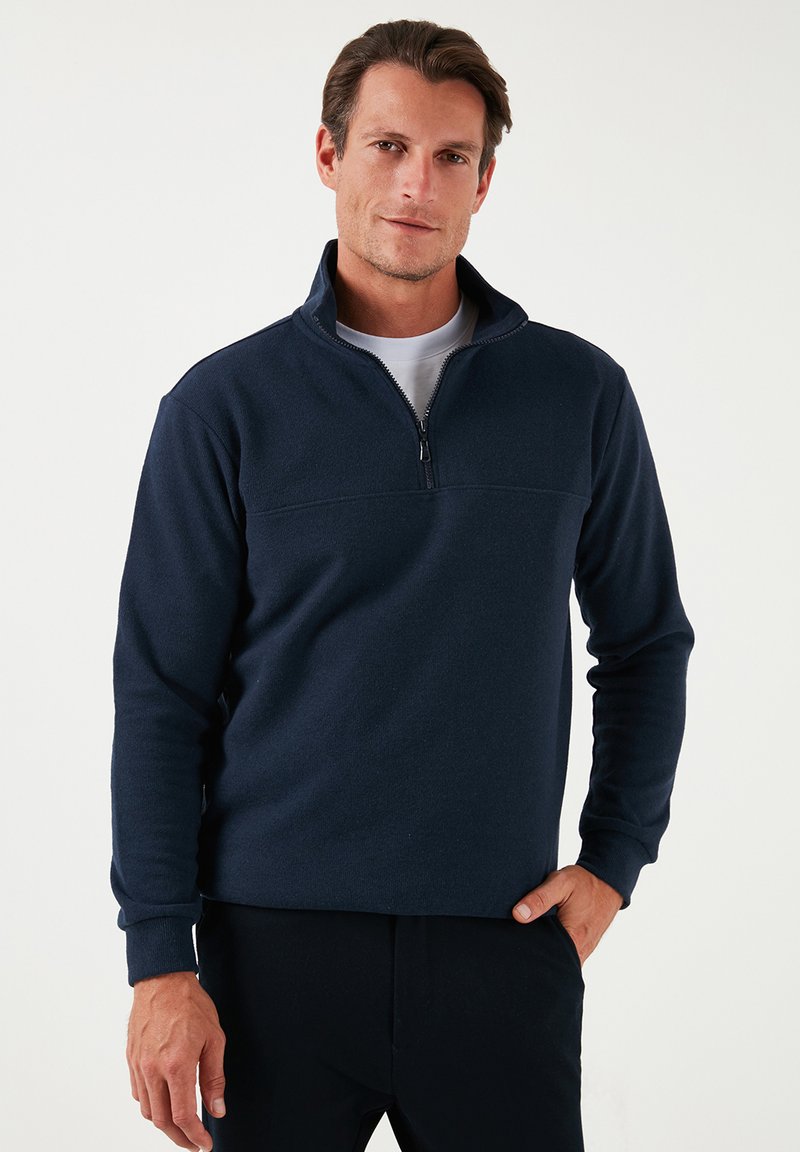 Pullover in pile blu scuro, con colletto a zip metà e maniche lunghe. Presenta una texture morbida e una cucitura orizzontale sul petto.