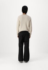 Lys beige striktrøje med lange ærmer, kombineret med løstsiddende sorte bukser med en baglomme. Enkle grå sko fuldender outfit'et.