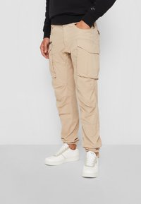 Beige cargo bukser med flere lommer, tapered manchetter og et let stof. Sammen med hvide sneakers for kontrast.
