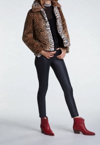 Veste en fausse fourrure imprimé léopard à la texture douce, pantalons noirs ajustés et bottines rouges à bout pointu et talon bas empilé.