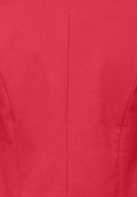 Gros plan sur un tissu rouge avec une couture centrale et des surpiqûres discrètes de contour sur un vêtement.