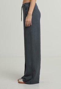 Grijze katoenen joggers met een elastische tailleband en trekkoord. Losse pasvorm, zijzakken en contrasterende stiksels. G gedragen met witte sneakers.