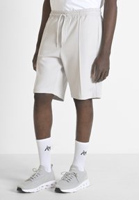 Shorts de sport gris clair avec une taille élastique et des poches latérales. Tissu texturé avec un logo subtil sur l'ourlet. Portés avec des baskets grises et des chaussettes blanches.