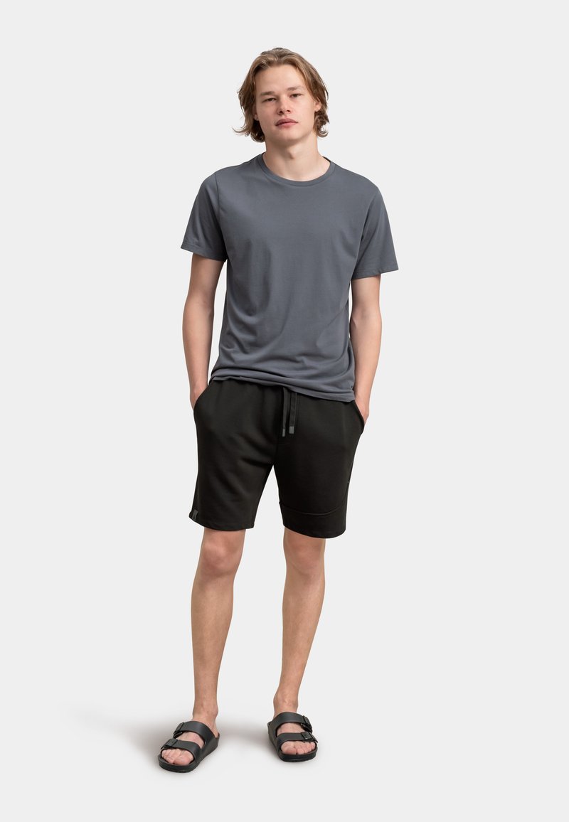 T-shirt grigio a maniche corte, pantaloni corti neri con cordino, e sandali neri. I materiali sembrano morbidi; i pantaloni corti hanno tasche laterali e una vestibilità rilassata.
