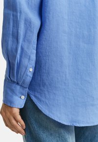 Lichtblauw linnen shirt met lange mouwen, met knoopsluiting aan de manchetten en een gebogen zoom, gecombineerd met denim jeans. Soepele structuur, casual ontwerp.