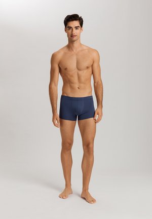 Marineblaue Boxershorts aus glattem Stoff mit einer taillierten Passform und einem elastischen Bund, Modell steht barfuß.