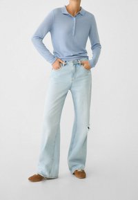 Hellblaues Langarm-Polohemd mit Knopfleiste, kombiniert mit weit geschnittenen hellen Jeans mit einer distressierten Detail. Braune Schuhe.