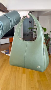 Zöld bőr kézitáska ívelt fogantyúval, sima textúrával és aranyszínű logóval. Csúszózsebbel és minimalista kialakítással rendelkezik.