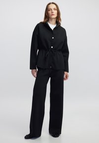 Zwarte, gestructureerde blouse met een getailleerde taille en lange mouwen, gecombineerd met een brede zwarte broek en versierde zwarte ballerina's.