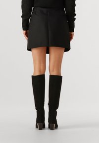 Zwarte minirok met een A-lijn vorm, voorzien van een soepele textuur en contrasterende stikdetails. Gecombineerd met zwart kniehoge laarzen.