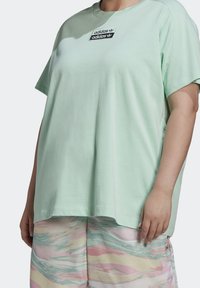 Světle zelené bavlněné tričko s krátkými rukávy a kulatým výstřihem, s černým logem Adidas na hrudi. Spárováno s kraťasy s barevným vzorem.