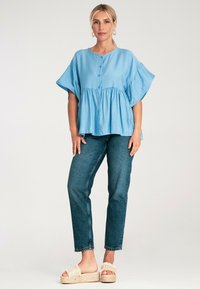 Jasnoniebieska bluzka z krótkim rękawem i zapięciem na guziki, luźny krój i ściągnięty w pasie. W połączeniu z ciemnoniebieskimi dżinsami i sandałami na platformie.