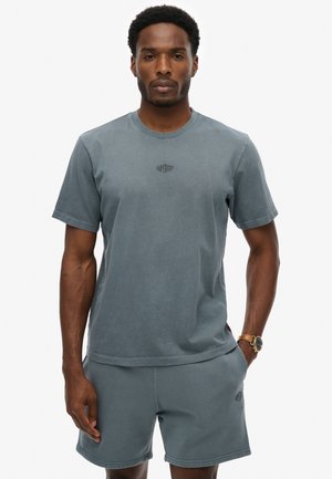 Camiseta de algodón gris con cuello redondo y un sutil logo en el pecho, combinada con pantalones cortos grises a juego que presentan un logo similar.