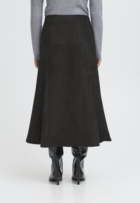 Gonna in suede nera con un design svasato, texture liscia e dettagli cuciti sul retro. Indossata con stivali neri al ginocchio lucidi.