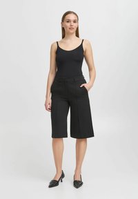 Juodas bodysuit'as ir juodos pločio kojų kelnės su kišenėmis. Kelnės pasižymi pritaikytu dizainu ir yra iki kelių ilgio. Juodi bateliai su smailiu nosiu.
