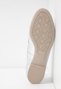 Baskets blanches avec une semelle en caoutchouc texturée présentant un motif géométrique, des détails de couture latéraux et la taille "37" embossée sur le côté.
