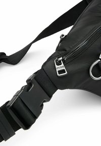 Borsa a tracolla nera in nylon con zip argentata, tracolla regolabile e fibbia in plastica. Texture liscia con dettagli hardware minimi.