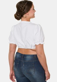 Hvid kortærmet bluse med puffede ærmer og blonder, parret med mørkeblå denim jeans med to baglommer og dekorativ syning.