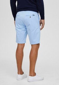 Lichtblauwe korte broek van een katoenmix, met twee achterzakken met knoopsluiting, gedragen met witte sneakers. Schoon, eenvoudig ontwerp.