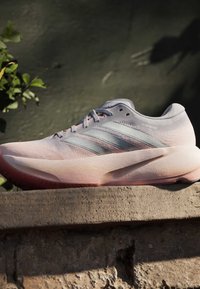 Ανοιχτό ροζ αθλητικό παπούτσι Adidas Primeknit με διαφανείς ρίγες, χοντρή σόλα και σχεδιασμό με κορδόνια σε πέτρινη επιφάνεια σε εξωτερικό χώρο.
