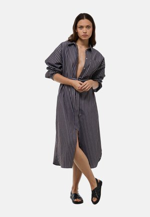 Robe chemise rayée avec col, dotée de longues manches et d'une fente latérale. Le tissu est sombre avec des rayures blanches contrastantes.