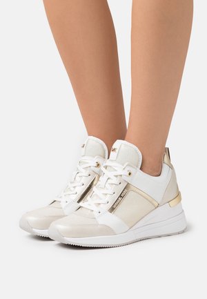 Baskets blanches et dorées avec un tissu texturé et du cuir lisse. Présentent des accents métalliques, un devant à lacets et une semelle rembourrée.
