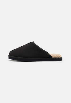 Zapatilla negra con un interior suave y texturizado, diseño tipo eslip y forma redondeada. Presenta una suela negra flexible.