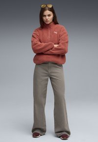 Pullover in pile rosso con zip a quarto, caratterizzato da un motivo testurizzato. Abbinato a jeans grigi larghi e sneakers bordeaux.