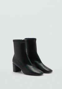 Bottines noires en matériau synthétique lisse, avec un bout pointu, un talon carré et une fermeture éclair sur le côté. Design minimaliste.