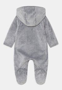 Combinaison en fausse fourrure grise avec capuche, présentant une texture douce, des manches longues et un design avec pieds. Dossier sans couture sans fermetures visibles.