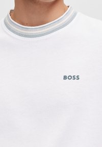 White cotton sweatshirt with a round collar. Features a textured ribbed trim and a small gray "BOSS" logo on the chest.