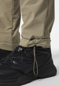Zwarte wandelschoenen met gestructureerde zijkanten en grijze veters, gecombineerd met kaki broeken met een koord aan de zoom.