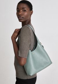 Mint green leather handbag with a slouchy design, featuring a gold logo, soft texture, and a single wide strap for shoulder wear.