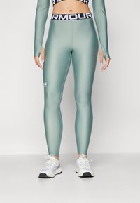 Hoge taille, getailleerde legging in matte teal materiaal met zwarte "ARMOUR" tailleband; beschikt over het Under Armour-logo nabij de enkel.