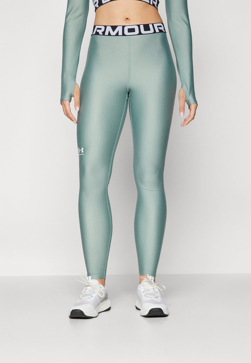 Hoge taille, getailleerde legging in matte teal materiaal met zwarte "ARMOUR" tailleband; beschikt over het Under Armour-logo nabij de enkel.
