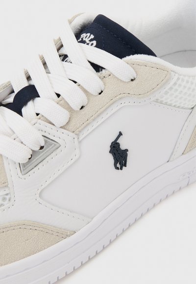 Άσπρο και μπεζ αθλητικό παπούτσι με λευκά κορδόνια, μαύρο λογότυπο Polo στο πλάι και μπλε γλώσσα με λευκό κείμενο Polo.