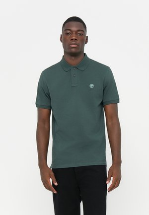 Polo shirt vert foncé en coton, avec un col à trois boutons et un logo discret sur la poitrine gauche. Manches courtes.