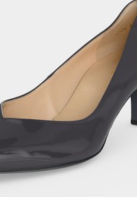 Chaussure à talon haut brillante noire avec un bout arrondi et une doublure intérieure beige vue en gros plan de côté.