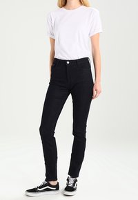 Mustat korkeavyötäröiset farkut, joissa on kapea malli, viisi taskua, edessä nappi kiinnitys ja sileä denimituntu, yhdistettynä valkoiseen T-paitaan.