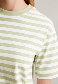 T-shirt en coton rayé vert clair et blanc avec un col rond et des manches courtes ; texture douce avec des motifs de rayures uniformes.