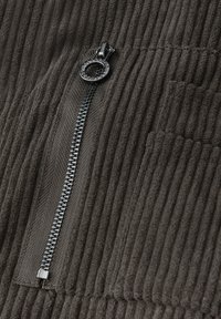Close-up van zwarte corduroy stof met verticale ribbels en een zwarte metalen ritssluiting met een ronde trekker.