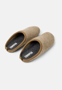Beige felt slippers with a brown rubber trim, rounded shape, black insole, and "CAMPER" branding on the insole. Textured surface.