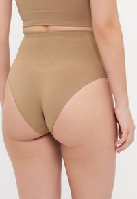 Mutande beige a vita alta, senza cuciture, con una texture liscia e cuciture minime, che mostrano un design a copertura totale.